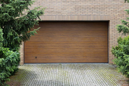 Wooden garage door closed, surrounded by brick wall and green pine trees.の写真素材