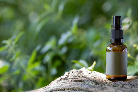 Amber glass spray bottle with blank label on rustic wooden surface, set against a natural outdoor...