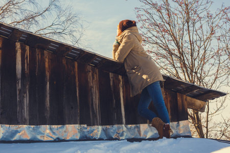 Thoughtful woman standing at the snowy roof while looking around on a sunny dayの写真素材