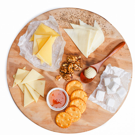 Variety of cheeses accompanied by walnuts,honey, crackers and butter roll on a round wooden plate.の写真素材