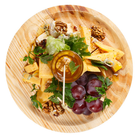 Cheese platter. Round wooden plate with variety of cheese accompanied by grape,honey, walnut and greens. Restaraunt foodの写真素材
