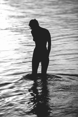 Silhouette of woman standing in river enjoying of sun setting.の写真素材