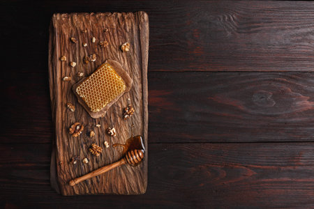 Honey dip, honeycomb and walnuts on carved wooden serving plate over burnished wood table. Top view, copy spaceの写真素材