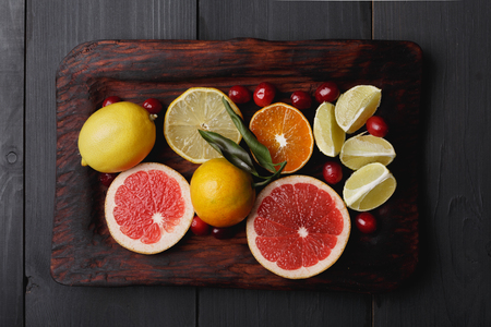 Ingredients for hot winter punch,sangria,toddy or mulled wine. Sliced lemon, grapefruit,tangerine, lime and cranberry on a rustic wooden tray over black wooden backdropの写真素材