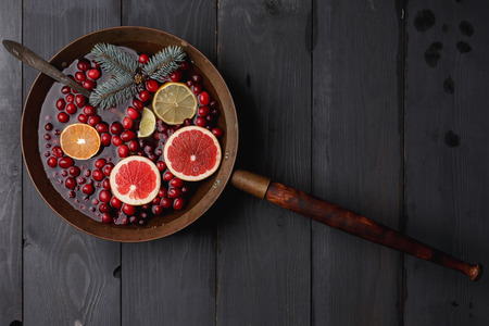 Hot winter punch,sangria,toddy or mulled wine with lemon, grapefruit,tangerine, lime and cranberry in aged rustic brass pot over black wooden tableの写真素材