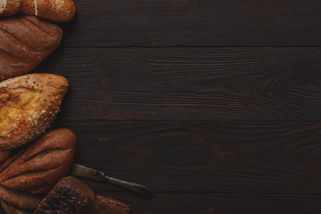 Different wholegrain breads on burnished wooden table. Flat lay, above view, chiaroscuro styledの写真素材