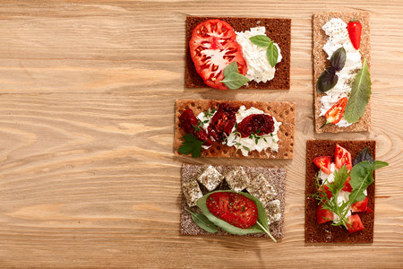 Different bread crisps (crispbread open-faced sandwiches) with both fresh and dried heirloom tomatoes, cream cheese and fresh greens. Above view, flat layの写真素材