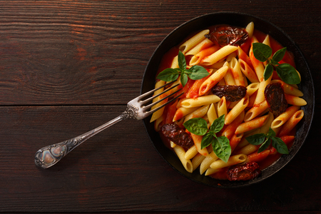 Pasta penne rigate with tomato sauce and basil leaves on wooden table. Top view, flat layの写真素材