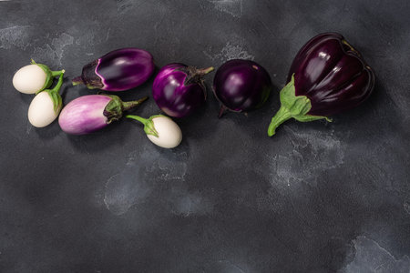 Aubergines or eggplants of different shapes and colors on dark grey background, top view, copy spaceの写真素材