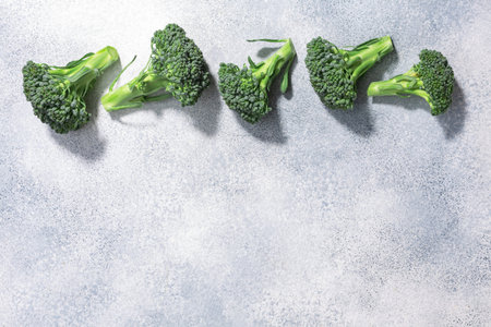 Broccoli flower heads atop light grey textured backdrop, copy space, top view