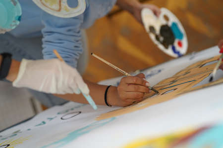 Hand in a rubber glove painting a picture with paints on canvasの写真素材