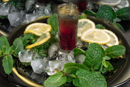 Cherry liqueur with mint and lemon on a black plate with iceの写真素材