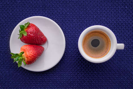 Two strawberries and a cup of coffee on a blue background, top viewの写真素材