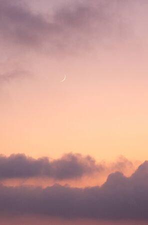 Cloudy orange evening sky and moonの写真素材