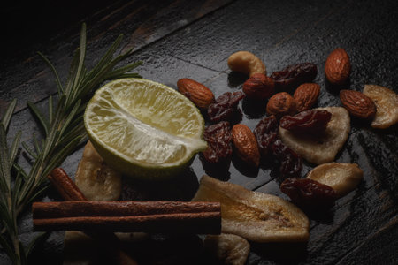 Mix of nuts, dried fruits and herbs on a black rustic background. Lime, canella, almond, raisins,...
