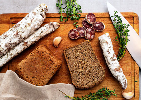 Fuet sausage on a cutting board with bread and herbs.の写真素材