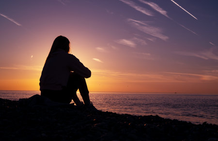 A girl is sitting on the beach watching the sunset. Silhouette of a girl.の写真素材