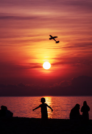 Boy launches an airplane into the sky at sunsetの写真素材