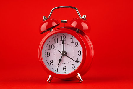 Red alarm clock on a red background. It's 7 o'clock on the clock. Morning.の写真素材