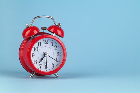 Red alarm clock on a light blue background. It's 7:30 o'clock on the clock. Morning. Place for text.の写真素材