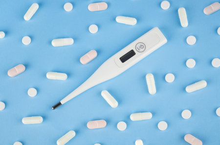 Digital thermometer with pills on a blue background. medical conceptの写真素材