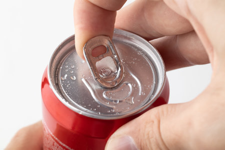 Close-up of a man's hand opening a red can of soda on a white background. A red can of soda opens.の写真素材