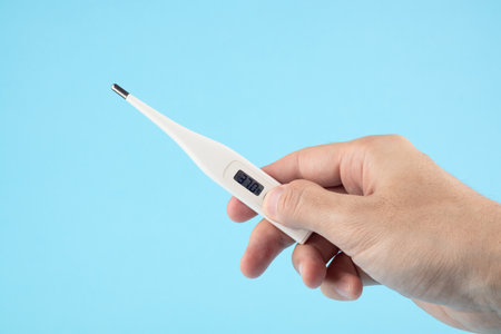 Male hands holding a digital thermometer with temperature 37 degrees on a blue background.の写真素材