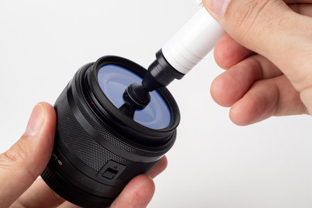 Cleaning digital camera lens, hands cleaning dust from front of lens with a special cleaning pencil, blurred background with lenses on the white surfaceの写真素材