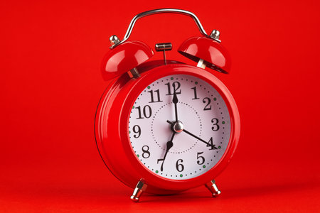 Red alarm clock on a red background. It's 7 o'clock on the clock. Morning.の写真素材