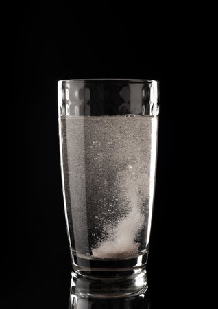 Effervescent pills. Glass with liquid in bubbles on a black background. aspirin. Tablet of vitaminsの写真素材