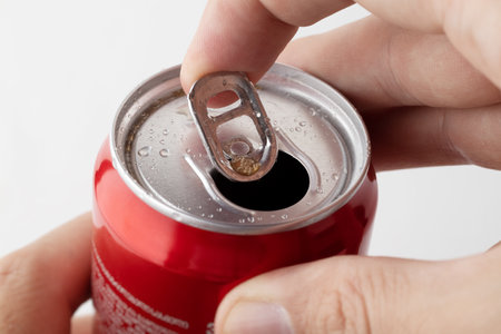 Close-up of a man's hand opening a red can of soda on a white background. A red can of soda opens.の写真素材