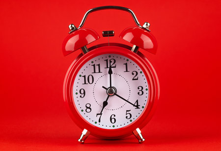 Red alarm clock on a red background. It's 7 o'clock on the clock. Morning.の写真素材