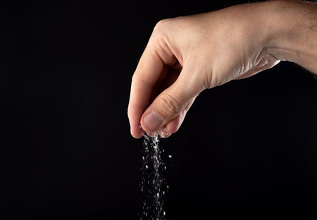 Hand sprinkling salt, salt on a black background.の写真素材