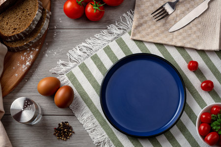 An empty blue plate as serving on the table. Table setting with vegetables and bread on a grey background.の写真素材