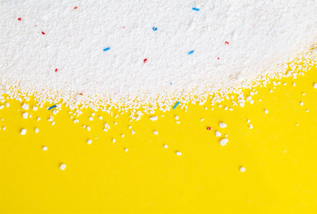 Washing powder with blue and red granules on a yellow background close up, top view.の写真素材