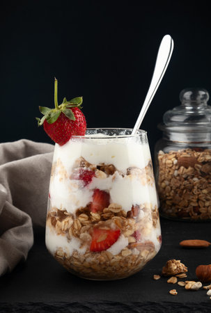 Greek yogurt with granola and strawberries in a glass on black backgroundの写真素材