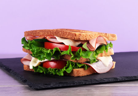 Sandwich with ham, cheese and vegetables on slate board on purple backgroundの写真素材
