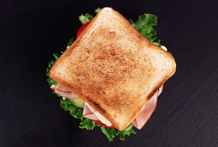 Sandwich with ham, cheese and vegetables on a black background.の写真素材