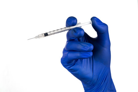 Syringe in hand in blue glove isolated on a white background.の写真素材