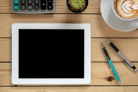 Office desk table with tablet blank screen,pens, coffee cup , and calculator .Top view with copy...