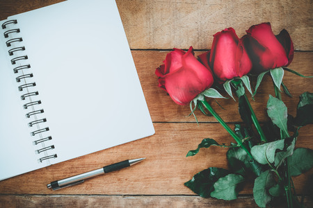 Red roses, leather notebook, pen and cup of coffee on wooden background with copy space.Valentines Day background concept, Wedding day.Top view vintage toneの写真素材