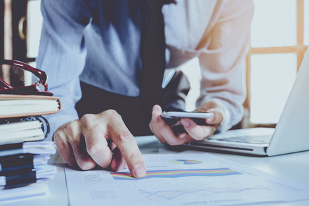 Businessman hand working  with business graph or analysis chart and using smart phone .Close up with sun flare.Business analysis and strategy concept.の写真素材