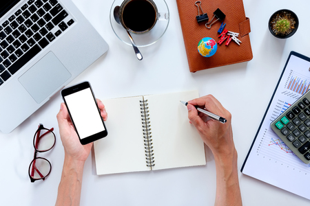 Businessman hands with pen writing notebook and holding blank screen smart phone on office desk table .View from above.Business analysis and strategy conceptの写真素材