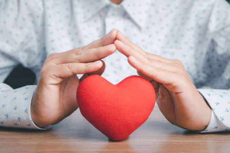 Red heart under hands in gesture of protection on wooden background, health care, love, organ donation, family insurance,CSR,world heart day, world health day, praying concept, Top view.の写真素材