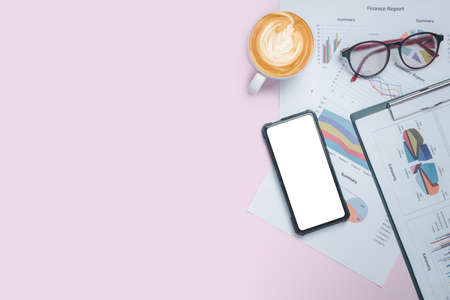 Pink office desk table with blank screen smart phone, eyeglass, analysis chart and cup of coffee .Top view with copy space.Office desk table concept.の写真素材
