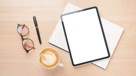 Office wooden desk workplace with blank screen tablet, notebook, pen, eyeglass and cup of coffee, Top view flat lay.の写真素材