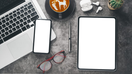 Dark office workplace with  blank screen tablet and smartphone, laptop computer, eyeglass, earphone,...