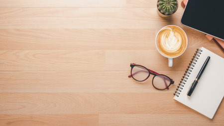Wooden desk workplace with notebook, pen, eyeglass, tablet and cup of coffee, Top view flat lay with copy space.の写真素材