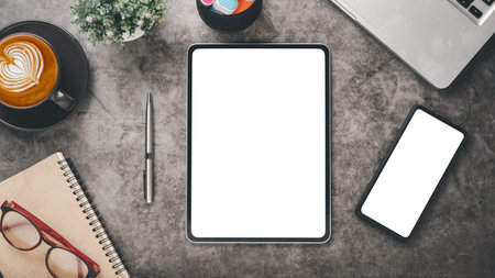 Office desk workplace with blank screen tablet and smartphone, laptop, pen, notebook, eyeglass and cup of coffee, Top view flat lay.の写真素材