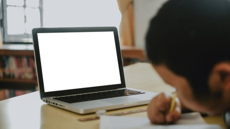 Blank screen laptop computer set up for work on wooden desk with boy doing homework background, Mockup, Empty screen, Blank screen for product display.の写真素材